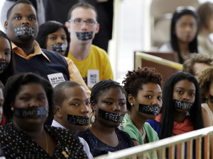 Members of North Carolina student chapters of the NAACP  and opponents of voter ID legislation wear tape over their mouths while sitting silently in the gallery of the House chamber of the North Carolina General Assembly where lawmakers debated and voted on voter identification legislation in Raleigh, N.C., Wednesday, April 24, 2013. (AP Photo/Gerry Broome)