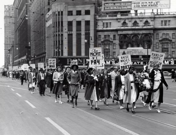 Members of the UAW Women’s Auxiliary march down Woodward Ave. and carry signs that denounce U.S. involvement in the Second World War and low worker wages, Detroit, Michigan.
