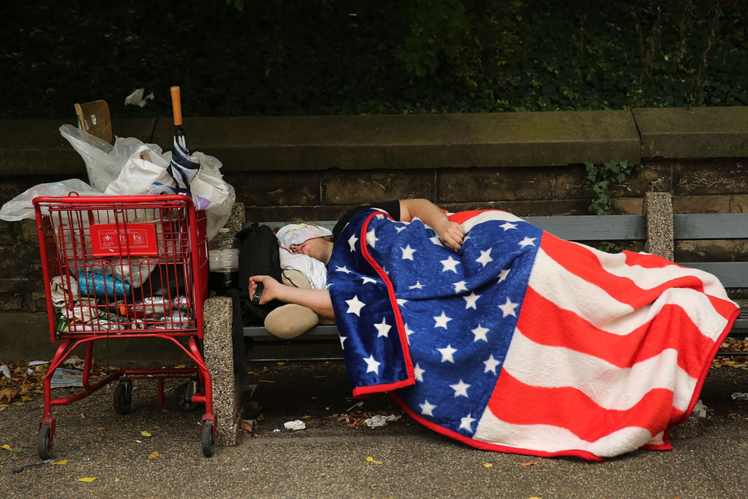 NEW YORK, NY - SEPTEMBER 10: A homeless man sleeps under an American Flag blanket on a park bench on September 10, 2013 in the Brooklyn borough of New York City. As of June 2013, there were an all-time record of 50,900 homeless people, including 12,100 homeless families with 21,300 homeless children homeless in New York City. (Photo by Spencer Platt/Getty Images) *** BESTPIX ***